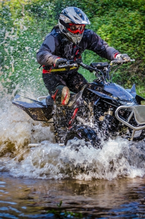 Quad rider through water stream in the forest.の写真素材