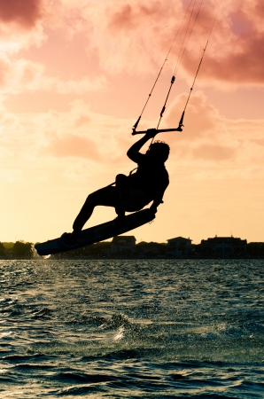Silhouette of a kitesurfer flying above the water at sunsetの写真素材
