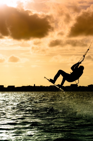 Silhouette of a kitesurfer flying above the water at sunsetの写真素材