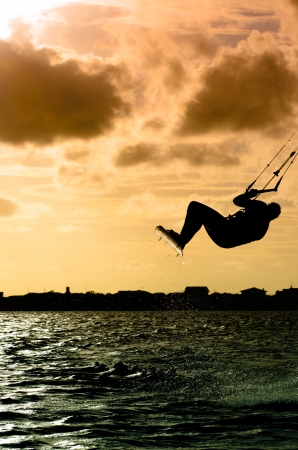 Silhouette of a kitesurfer flying above the water at sunsetの写真素材
