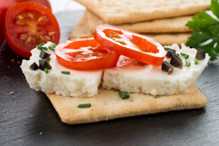 Crispbread with fromage, tomato and olives on black ardoise tray.の写真素材