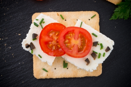 Crispbread with fromage, tomato and olives on black ardoise tray.