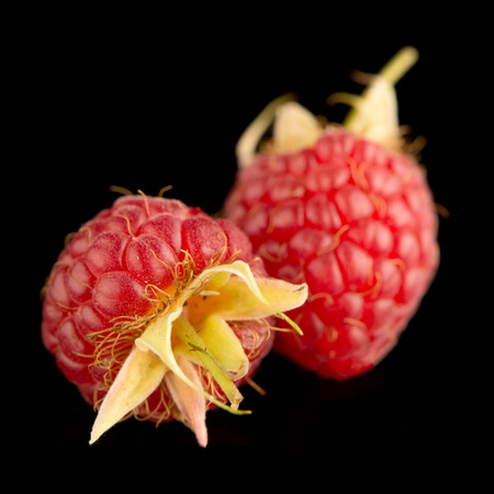 Fresh raspberries on black reflective background.