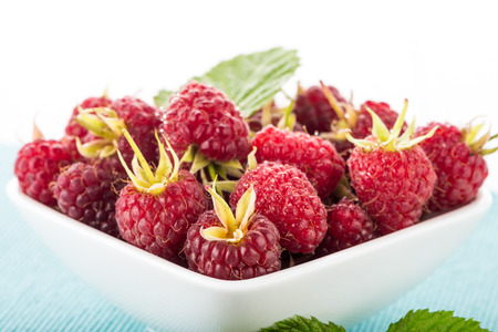 Fresh raspberry in a white bowl on wooden table.