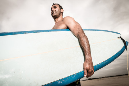 Surfer wathing the waves on the beach with his surfboard.の写真素材