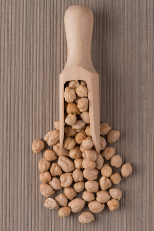 Top view of wooden scoop with chickpeas against beige vinyl background.の写真素材