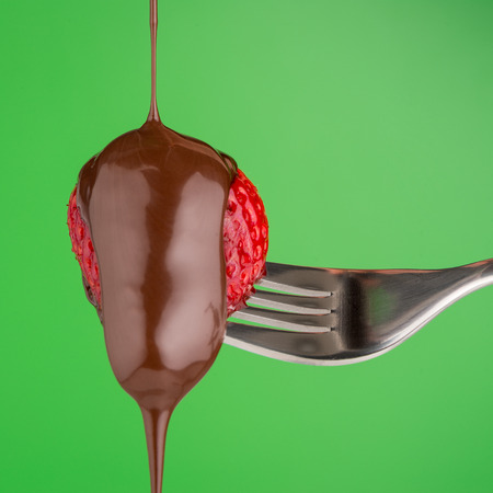 Strawberry and chocolate on a fork on green background.の写真素材
