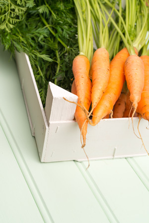 Carrots inside white wooden box on the light green wooden table.の写真素材