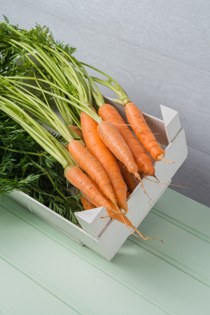 Carrots inside white wooden box on the light green wooden table.の写真素材