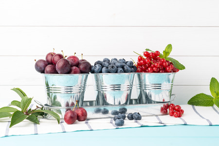 Plums, red currants and blueberries in small metal bucket on the wooden table.の写真素材