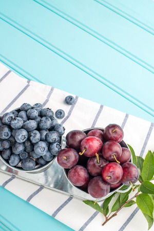 Plums, and blueberries in small metal bucket on the wooden table.の写真素材