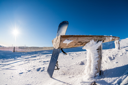 Snowboard leaning on a wood rail on a winter snow covered mountainside and sun shine in blue sky.の写真素材