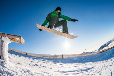 Snowboarder jumping from a wood rail against blue sky.の写真素材