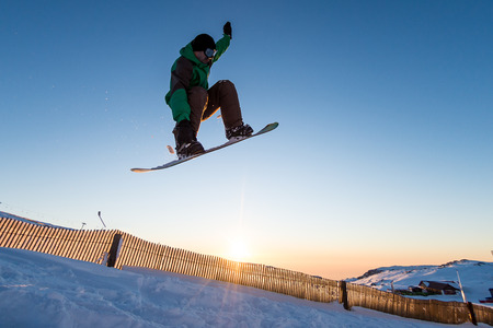 Snowboarder at jump in mountains at sunset sky.の写真素材