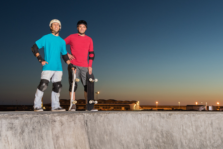 Two skateboarders standing near a concrete pool at skatepark on a beatiful sunset.の写真素材