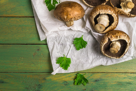 Fresh uncooked brown mushrooms and parsley leaves branch on rustic wooden green painted background.の写真素材