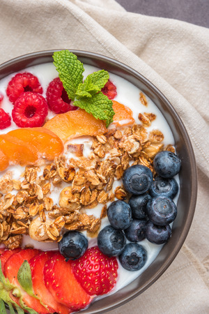 Yogurt with baked granola and berries in small bowl strawberries blueberries. Granola baked with nuts and honey for little sweetness.の写真素材