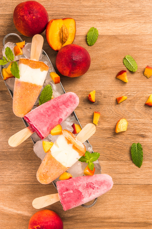 Homemade raspberries and peach popsicles on a wooden table.の写真素材