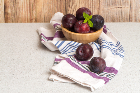 Delicious red plums in a wooden bowl on kitchen countertop.の写真素材