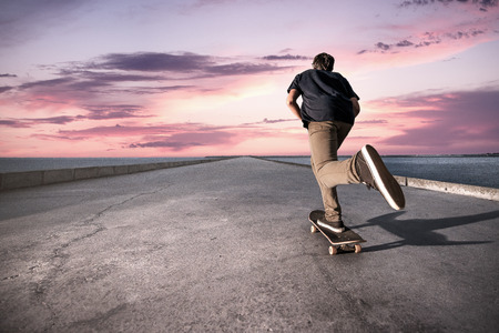 Skateboarder pushing on a concrete pavement along the harbour during the sunset.の写真素材