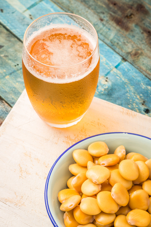 Tasty lupins in metal mug and glass of beer on wooden table top.の写真素材