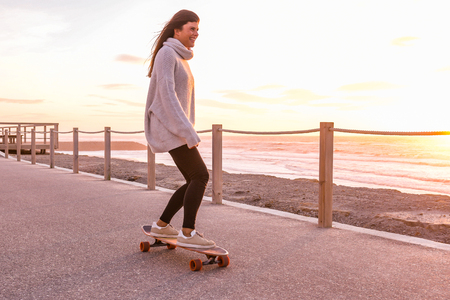 Girl riding a skateboard near the beach at sunset.の写真素材