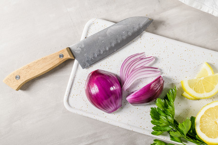 Sliced red onion, lemon and parsley leaves on white ceramic cutting board.の写真素材