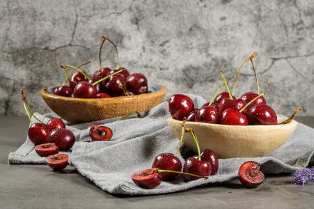 Red fresh cherries in bowls and a bunch of cherries on the table.の写真素材