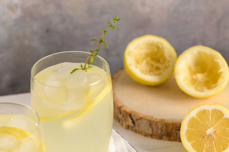 Cold lemonade or alcoholic cocktail with lemon, rosemary and ice in glass glasses on a light background.の写真素材