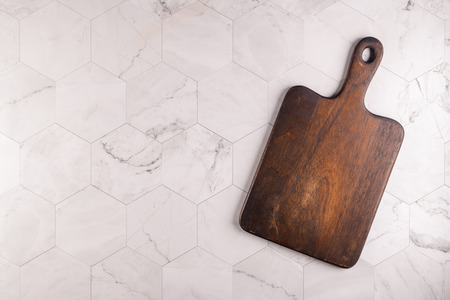 Wooden cutting board on a light gray hexagonal marble tiles background. Top view. Copy space for...