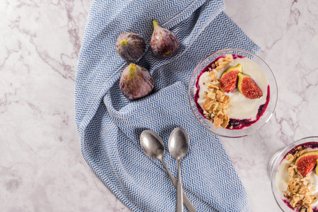 Figs pudding parfait with yogurt, blueberry jam, figs, hazelnut, and cookies in glass on white...