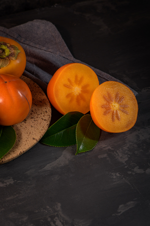 Ripe persimmon fruits in a cork plate on dark kitchen counter top.の写真素材