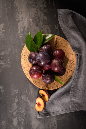 Delicious red plums in a cork plate on kitchen countertop.の写真素材