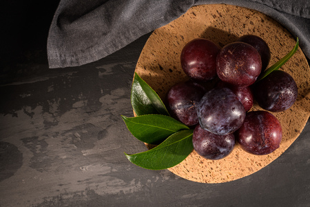 Delicious red plums in a cork plate on kitchen countertop.の写真素材