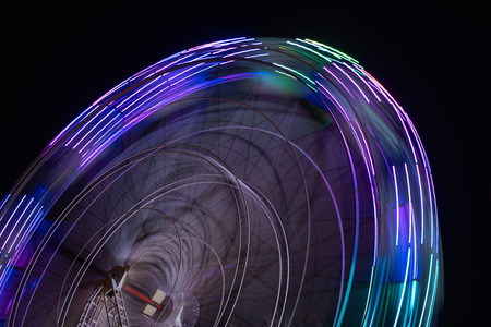 Colourful striped light illuminated spinning ferris wheel in motion moving at night.