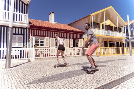 Young active couple enjoying a summer sunny day skateboarding near typical Costa Nova houses in Aveiro - Portugal.の写真素材