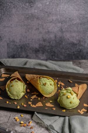 Balls of pistachio ice cream in waffle cones on a dark background.