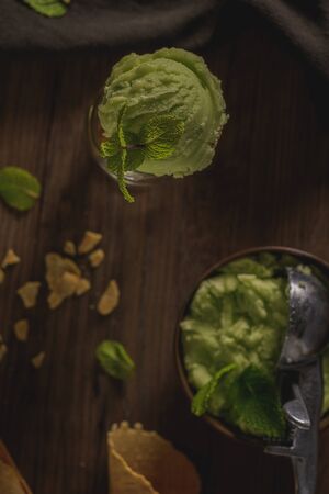 Pistachio ice cream in a dark rustic bowl and waffle cone on a brown wooden background.の写真素材