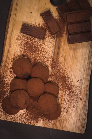 Craft chocolate truffles on wooden board with cocoa powder.