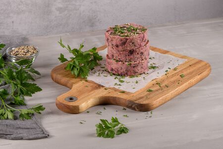 Raw veggie burger with beetroot and white beans with parsley leaves on wood cutting board.