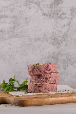 Raw veggie burger with beetroot and white beans with parsley leaves on wood cutting board.