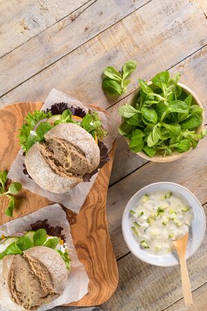 Healthy vegan burger with fresh vegetables and yogurt sauce on rustic kitchen counter top.の写真素材