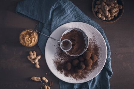 Craft chocolate truffles on plate with cocoa powder and peanuts.