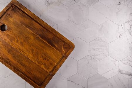 Top view of wooden cutting board on modern hexagonal pattern marble stone countertop.