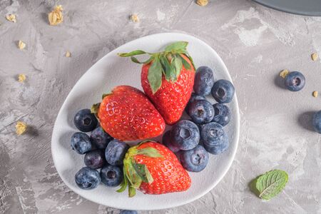 Organic fresh berries of strawberry, blackberry on a white plate on a light grey concrete background. Healthy eating Vegetarian diet.の写真素材