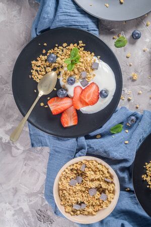 Ripe blueberries and strawberries with yogurt and granola in plate on a light grey background. Healthy Eating.の写真素材
