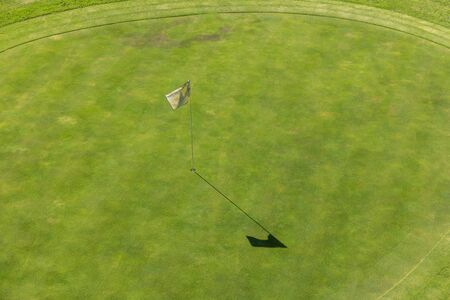 Aerial view of a golf course. In detail you can see the lawn of the hole and white flag of signaling. The sun shines and is an ideal day for sports and outdoor activities.の写真素材