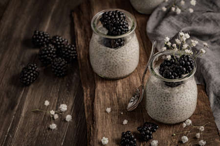 Chia pudding with blackberries, three portions in glass jars on a dark table.の写真素材