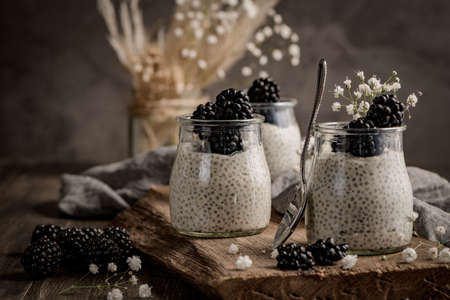 Chia pudding with blackberries, three portions in glass jars on a dark table.の写真素材