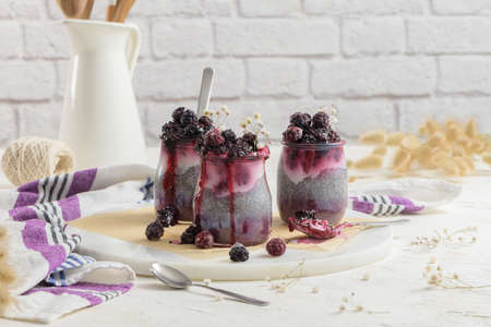 Chia pudding with blackberries, three portions in glass jars on a white table.